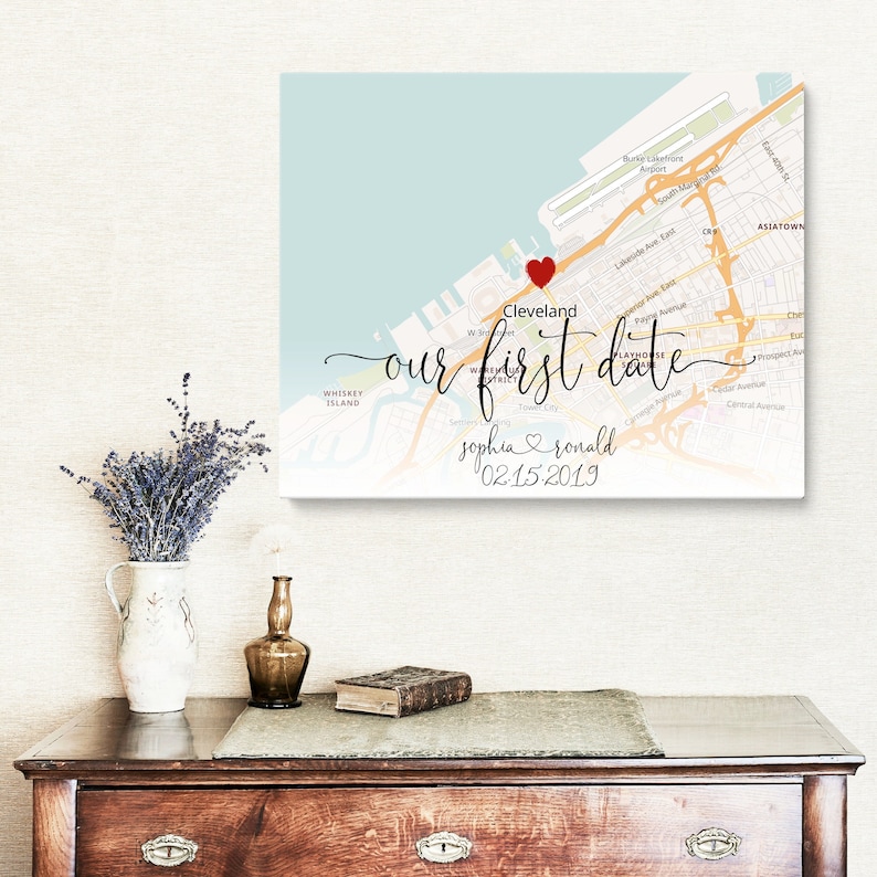 Puede incluir: Una impresi&oacute;n de mapa con un coraz&oacute;n rojo que marca la ubicaci&oacute;n de Cleveland, Ohio. El texto "our first date" est&aacute; escrito en cursiva, junto con los nombres "sophia & ronald" y la fecha "02-15-2019".