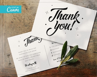 May include: Two white thank you cards with black script text and decorative elements. One card reads "Thank You!" in large script. The other card includes a thank you message, discount code, and shop details. A sprig of green leaves rests on the cards.
