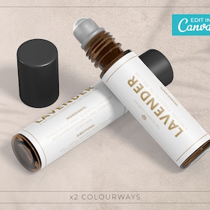 Op de afbeelding: Twee bruine glazen rollerflessen met witte etiketten waarop "Lavender" en "A Natural Essential Oil Roll-On" staat. De flessen staan op een lichtbruin, zanderig oppervlak.