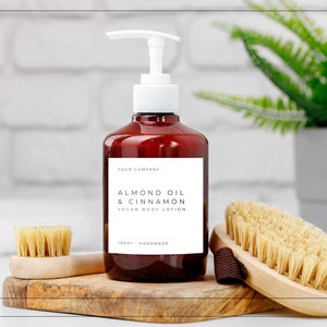 May include: A brown bottle with a white pump dispenser filled with almond oil and cinnamon vegan body lotion. The bottle has a white label with the text "Your Company, Almond Oil & Cinnamon, Vegan Body Lotion, 150ml - Handmade".