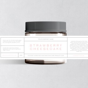 May include: A glass jar with a black lid and a label that reads "STRAWBERRY CHEESECAKE" in pink lettering. The label also includes the text "YOUR COMPANY NAME" and lists ingredients for a handmade skin care product.