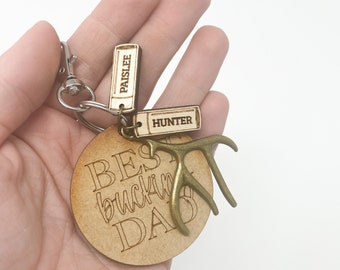 May include: Wooden keychain with a round tag that says "Best Buckin' Dad" with a small antler charm. The keychain also has two smaller wooden tags with the names "Paislee" and "Hunter" engraved on them.