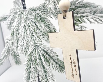 May include: A light-colored wooden cross ornament featuring two round wooden beads on a jute twine hanger. The surface of the cross is engraved with the text "the scarlet thread Proverbs 31:21" in a dark script font along the bottom right arm.