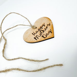 May include: A wooden heart-shaped tag with the text "Happy Mother's Day" engraved on it. The tag is attached to a piece of twine.