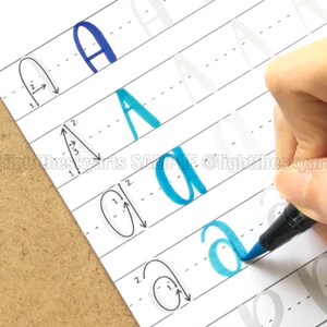 May include: A hand holding a blue marker is writing the letter "a" on a lined paper. The paper shows examples of the letter "A" in different styles, with numbered stroke guides. The text "@lighttheskyarts SAMPLE @lighttheskyarts" is visible.
