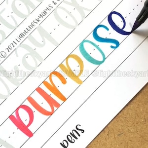 May include: A close-up of a white paper with the word "Purpose" written in colorful calligraphy. The word is written in shades of red, orange, yellow, teal, and blue. The image also includes the text "@lighttheskyarts SAMPLE @lighttheskyarts".