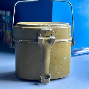 May include: A green metal camping mess kit with a hinged lid and a carrying handle. The kit has a worn, vintage look.