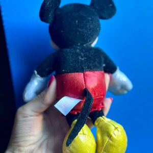 May include: A black and red plush Mickey Mouse toy with yellow shoes. The toy has a tag on its back that says "Disney Baby".