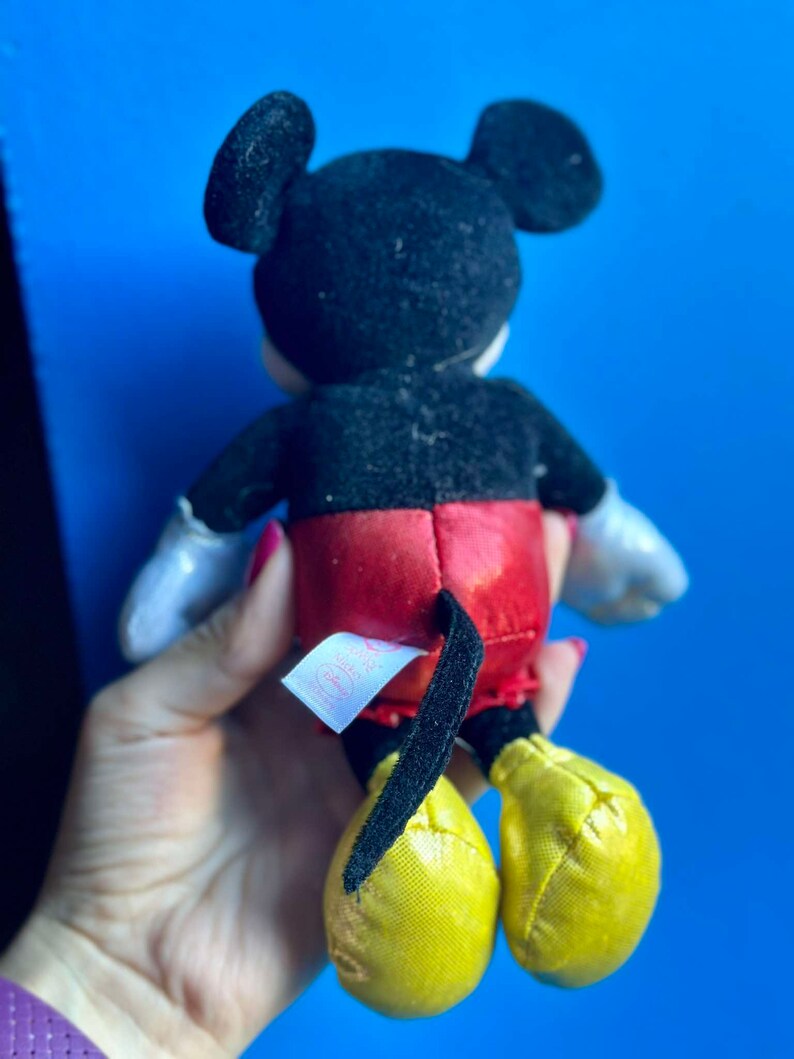 May include: A black and red plush Mickey Mouse toy with yellow shoes. The toy has a tag on its back that says "Disney Baby".