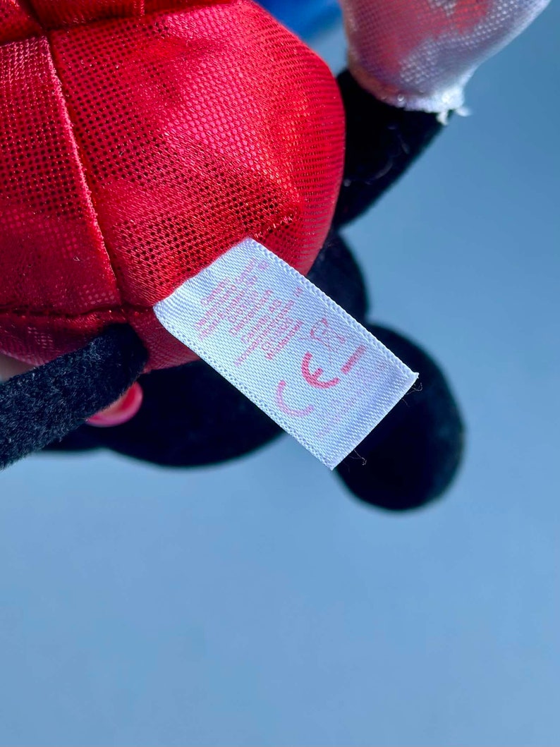 May include: Red and black plush toy with a white tag that says "CE".