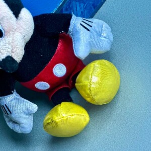 May include: A black and red plush Mickey Mouse toy with yellow ears and white gloves. The toy is lying on a blue surface.