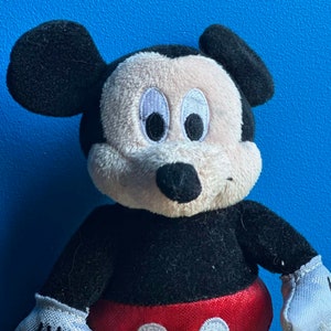 May include: A plush black and white Mickey Mouse toy with large black ears and a red and white polka dot bow tie.