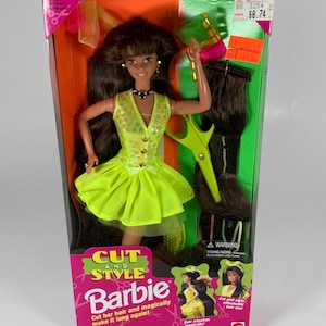 May include: A Barbie doll in a box, featuring a neon green dress and long brown hair. The box includes a pair of green scissors and additional hair extensions. The packaging reads "Cut and Style Barbie".