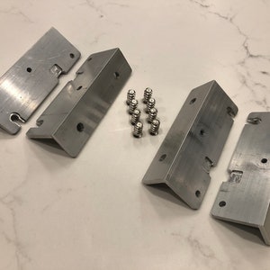 May include: Four silver metal brackets with eight silver screws. The brackets have holes for screws and a slot for a hinge.