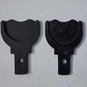 May include: Two black plastic parts with a unique shape. Each part has a curved top with a semi-circular indentation and a rectangular base with a circular hole. One part has the letters "A" and "B" embossed.