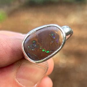 May include: A white ceramic mug with a black handle and the text "But First, Coffee" in a bold, black font. The mug is set against a blurred background, suggesting a cozy setting.