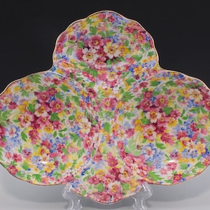 May include: A three-sectioned serving dish with a floral pattern in shades of pink, yellow, blue, and green. The dish has a gold rim and is made of ceramic.