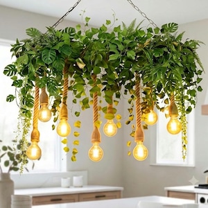 May include: A hanging chandelier featuring a circular frame covered in lush green artificial foliage, including monstera and fern leaves. Six light bulbs are suspended from the frame by thick, tan twisted rope cords, emitting a warm glow.