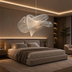 May include: A large, sculptural pendant light fixture with a translucent, flowing, cloud-like shade made of layered, sheer white fabric. The light is suspended from the ceiling by a thin cord, emitting a soft, diffused glow over a bedroom.