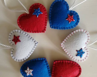 May include: Six felt heart ornaments in red, white, and blue with white stars. Each heart has a white string loop for hanging.