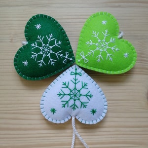 3 green and white christmas tree ornaments. all are felt hearts with hand embroidered snowflake. snowflake is in the center of the heart, and asides are two sparkles. snowflake is white on green hearts, and green on white heart, ends with a ribbon.