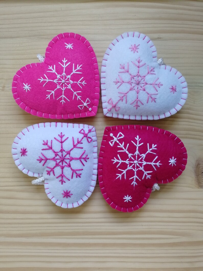 4 pink and white christmas tree ornaments. all are felt hearts with hand embroidered snowflake. snowflake is in the center of the heart, and asides are two sparkles. snowflake is white on pink hearts, and pink on white hearts, ends with a ribbon.