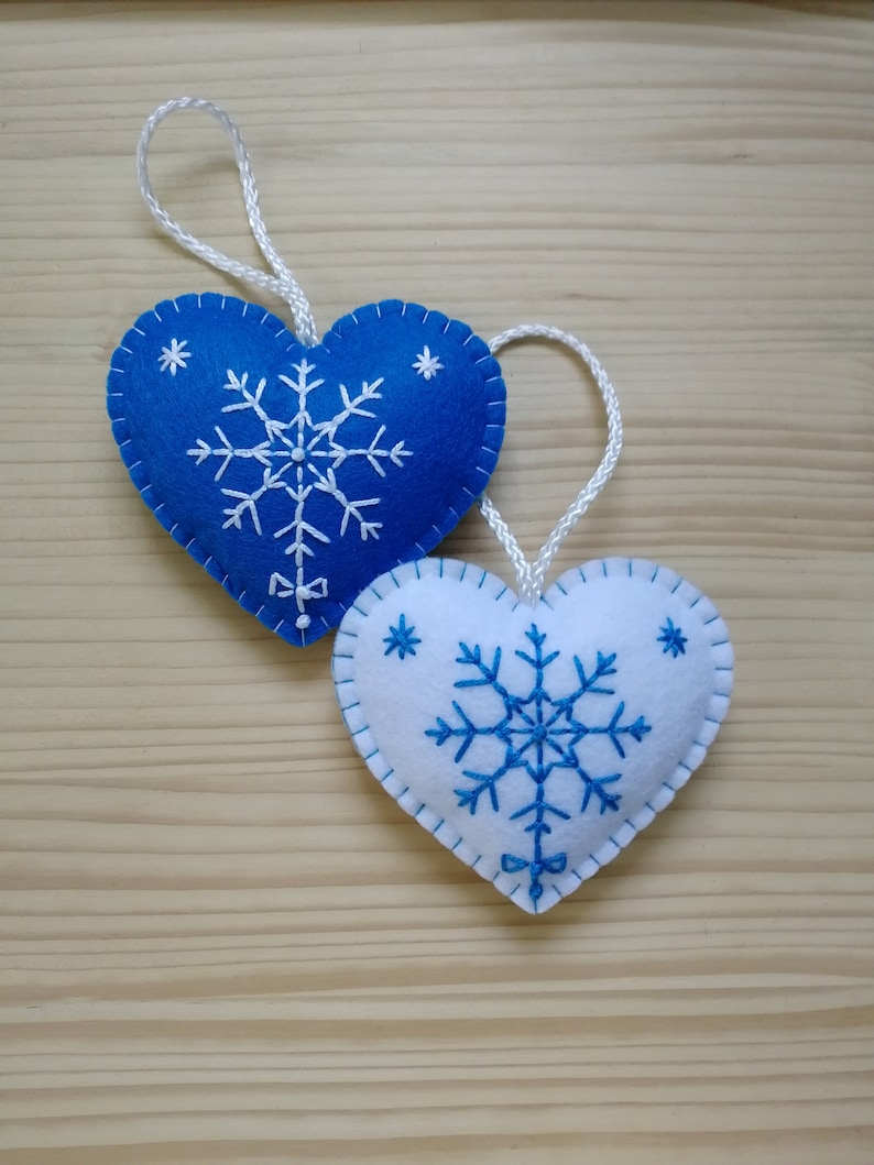 royal blue and white christmas tree ornaments. both are felt hearts with hand embroidered snowflake. snowflake is in the center of the heart, and asides are two sparkles. snowflake is white on blue heart, and blue on white heart. Ends with a ribbon.