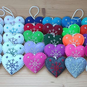 A collection of heart-shaped ornaments in various colors, including white, blue, red, green, orange, purple, pink, gray, and teal. Each ornament features a snowflake design and a white string for hanging. These ornaments are perfect for winter or holiday decor.