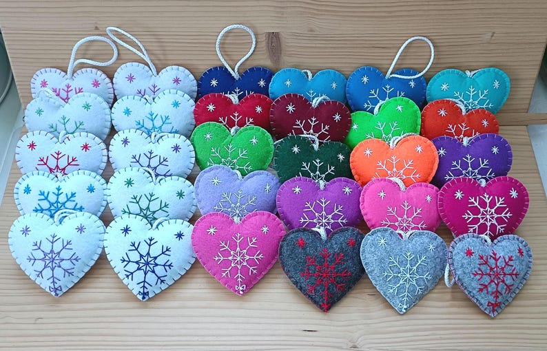 A collection of heart-shaped ornaments in various colors, including white, blue, red, green, orange, purple, pink, gray, and teal. Each ornament features a snowflake design and a white string for hanging. These ornaments are perfect for winter or holiday decor.