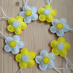 May include: Seven felt flower ornaments in yellow and white with white stitching. Each flower has a loop for hanging.