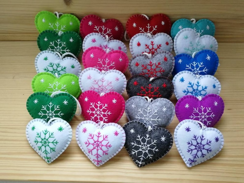 winter and christmas decoration, handmade from felt. twenty four felt hearts with hand embroidered snowflake are set on a display board. these are christmas tree ornaments in wide variety of colors. hearts are plush and with string. lovely.