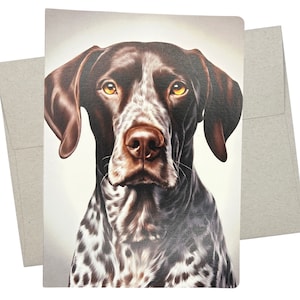 May include: A greeting card featuring a detailed portrait of a German Shorthaired Pointer. The dog has brown and white spotted fur, with a brown nose and large, expressive yellow eyes. The card is accompanied by a plain, light-colored envelope.