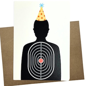 May include: A greeting card featuring a black silhouette of a person with a target design on the torso. The person is wearing a party hat with orange polka dots. The card is paired with a brown envelope.
