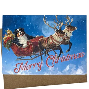 May include: A Christmas card featuring a Bernese Mountain Dog in a red sleigh pulled by two reindeer against a blue sky with a full moon. The words "Merry Christmas" are written in red script.