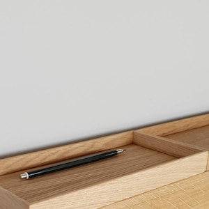 Op de afbeelding: Een lichtgekleurde houten bureau-organizer met een rechthoekige pennenbak en een apart compartiment. Een zwarte pen met een zilveren punt ligt in de bak. De houtnerf is zichtbaar.