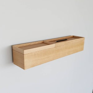 Op de afbeelding: Een lichtgekleurd, rechthoekig zwevend houten rek met een verzonken bovendeel en een apart dienblad. Een zwarte pen ligt op de plank. De plank is aan een witte muur bevestigd. De plank is ongeveer 100 cm lang.