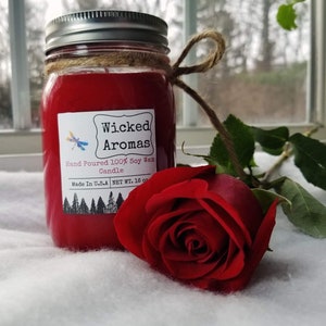 May include: A red soy wax candle in a glass jar with a silver lid. The jar has a label that reads "Wicked Aromas" and "Hand Poured 100% Soy Wax Candle". The candle is next to a red rose.