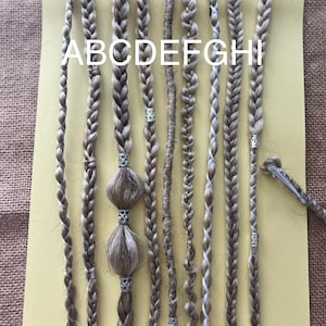 Può includere: Nove trecce diverse di extensioni per capelli, etichettate dalla A alla I, sono esposte su uno sfondo giallo. Le trecce sono di colori e trame diverse, e alcune hanno perline o altri abbellimenti.