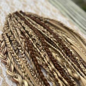 May include: A collection of brown and blonde synthetic hair braids. The braids are arranged in a fan shape and are ready to be used for hair extensions.