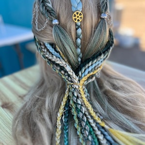 May include: A blonde wig with multiple braids in shades of blue, green, and yellow. The braids are tied together with silver beads and a gold charm.