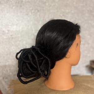 May include: A mannequin head with black hair styled in a bun. The hair is tightly woven and secured at the nape of the neck. The mannequin has a tan complexion and is set against a neutral background.