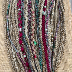 May include: A collection of synthetic hair braids in various shades of brown, red, and green. The braids are decorated with beads and charms, including a snowflake charm.