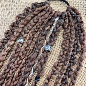 May include: A set of brown and black braided hair extensions with silver beads and a black elastic band.