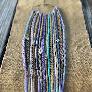 May include: A set of synthetic hair extensions in shades of brown, purple, and teal. The extensions are braided and have small decorative charms attached.