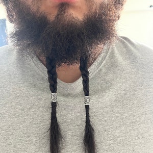 May include: A man with a braided beard wearing silver beads with a rune symbol on each bead.