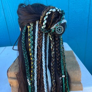 May include: A long, dark brown wig with multiple braids in various colors, including green, white, and brown. The braids are tied together with a silver gear charm.