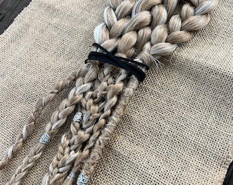 May include: A set of four blonde braids with white highlights, tied together with a black elastic band. The braids are decorated with silver beads.