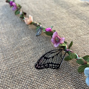 May include: A twig wrapped in pink, blue, and green yarn with small fabric flowers and a black butterfly charm.