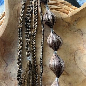 Può includere: Quattro ciocche di extensioni per capelli intrecciati in tonalità di marrone e oro, con alcuni fili neri. Le extensioni sono legate insieme con elastici trasparenti. Ci sono anche cinque ciocche di capelli marroni e bianchi legate insieme con elastici trasparenti.