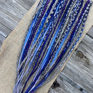 May include: A set of blue, purple, and gray synthetic hair extensions. The extensions are braided and ready to be installed.